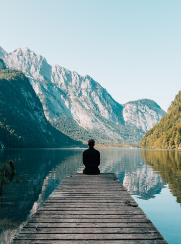 person sitting at end of dock looking at gorgeous water and mountain scene